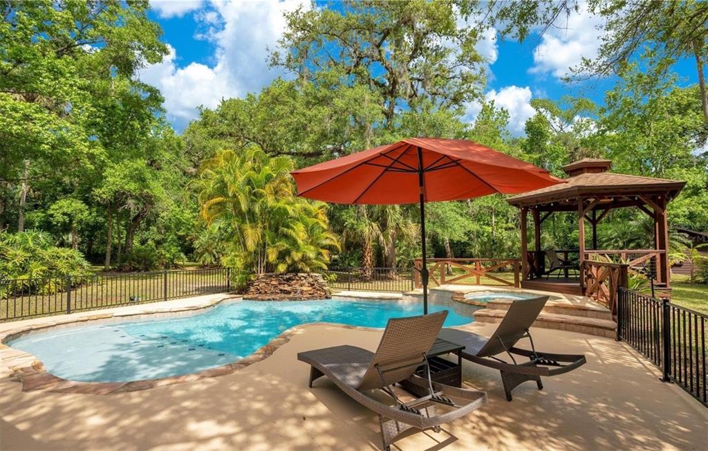 A swimming pool with a stone waterfall, lounge chairs, and a wooden gazebo outdoors — 120 E BAHAMA ROAD, WINTER SPRINGS, FL