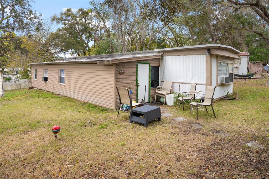 A tan mobile home with a small patio area featuring outdoor chairs and a side table — 2107 HIALEAH AVENUE, LEESBURG, FL