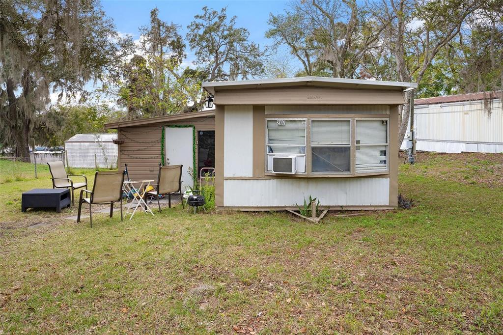 A brown and white mobile home sits on a grassy lot with outdoor patio furniture — 2107 HIALEAH AVENUE, LEESBURG, FL