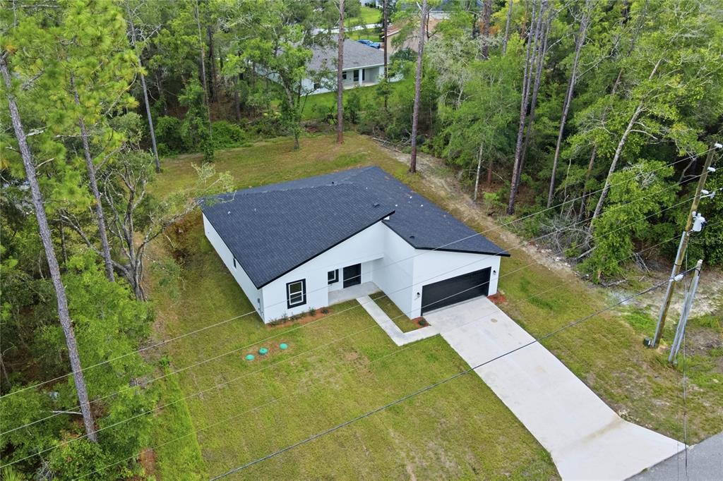 An aerial view shows a modern white house with a black roof and attached garage — 8809 N CIRCULAR WAY, CITRUS SPRINGS, FL