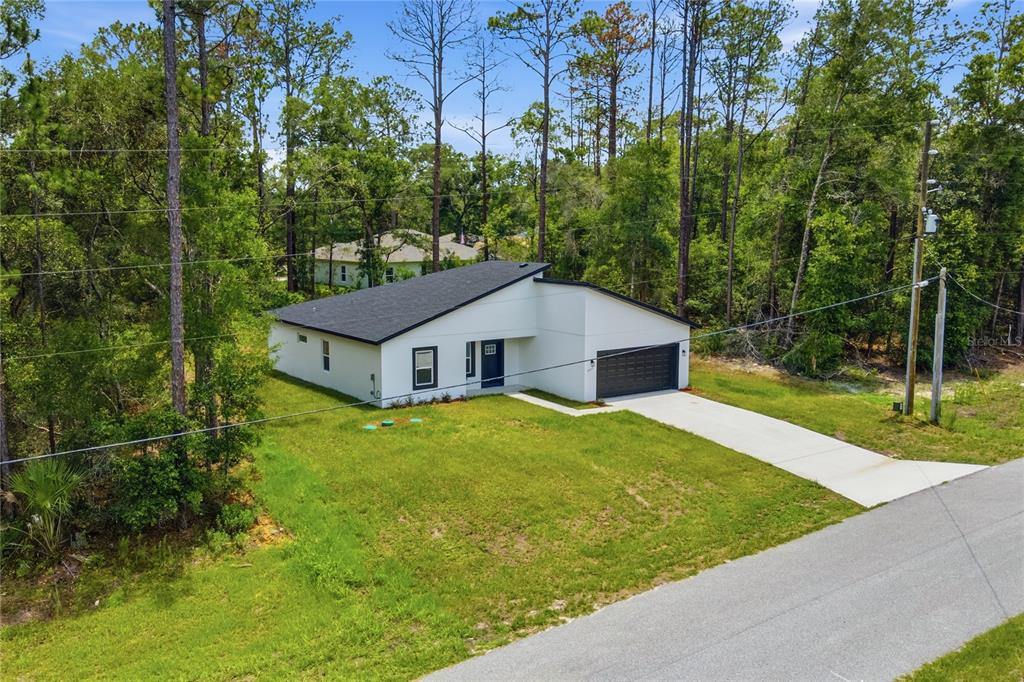 A modern white single-story house with a black roof and garage sits among tall trees — 8809 N CIRCULAR WAY, CITRUS SPRINGS, FL