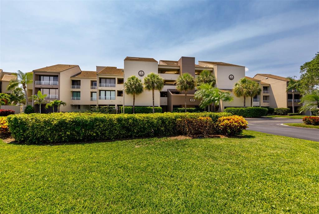 A multi-story apartment building with beige stucco walls sits behind a manicured lawn and hedge — 2775 KIPPS COLONY DRIVE S UNIT 304, ST PETERSBURG, FL