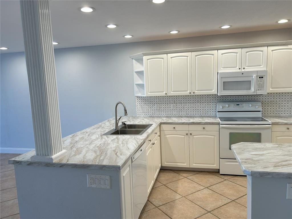 A kitchen features white cabinets, marble-patterned countertops, a stainless steel sink, and tile flooring — 2775 KIPPS COLONY DRIVE S UNIT 304, ST PETERSBURG, FL