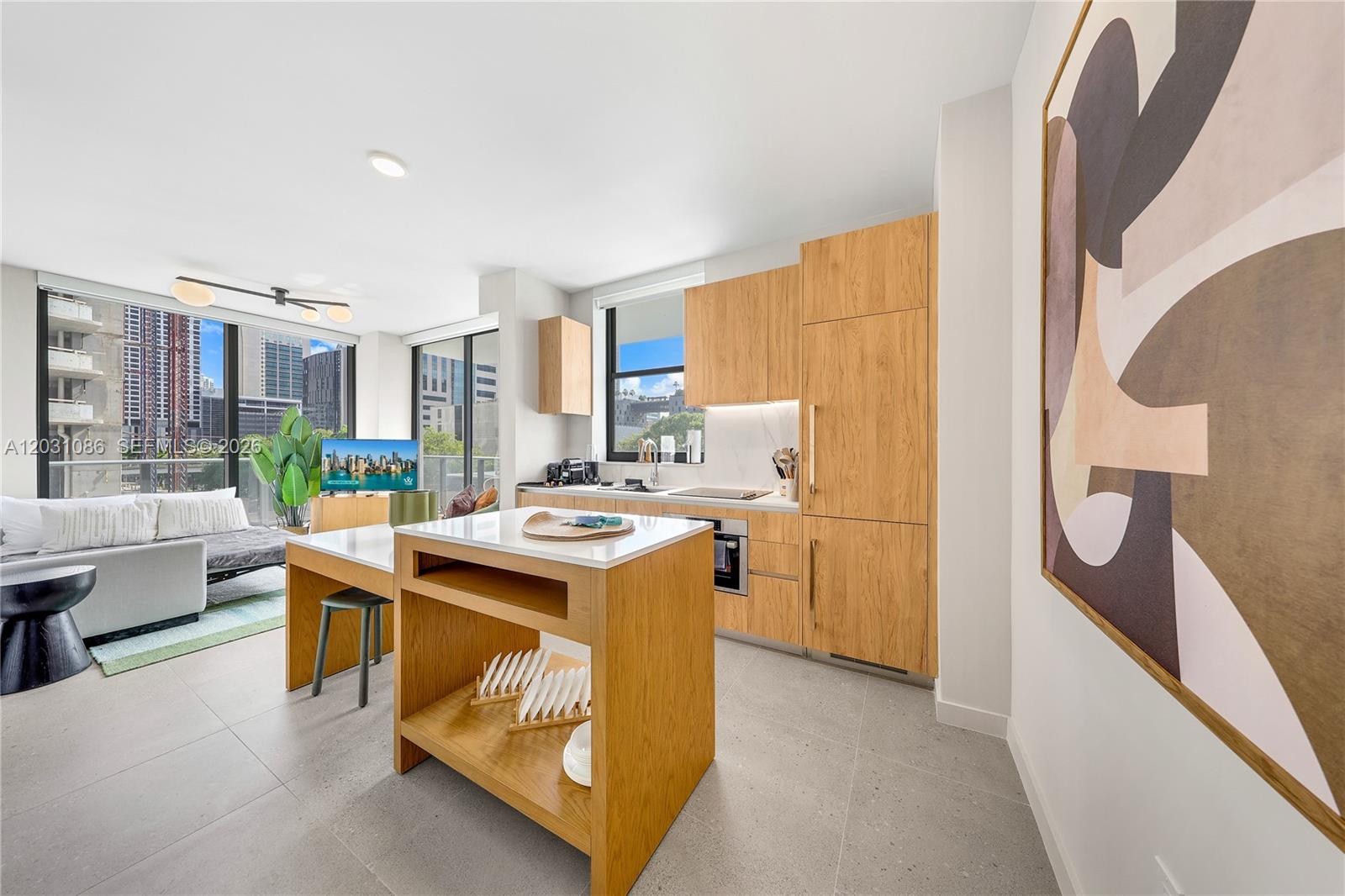 A modern kitchen and living area feature light wood cabinetry, a central island, and balcony views — 11 NE 6th St # 301, Miami FL 33132, MIAMI, FL