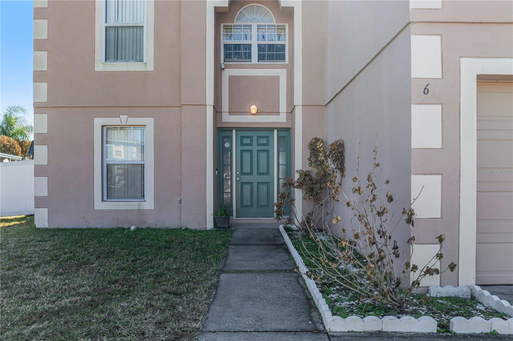 A two-story house exterior features a teal front door, a concrete walkway, and a garage — 6 ALICANTE COURT, KISSIMMEE, FL