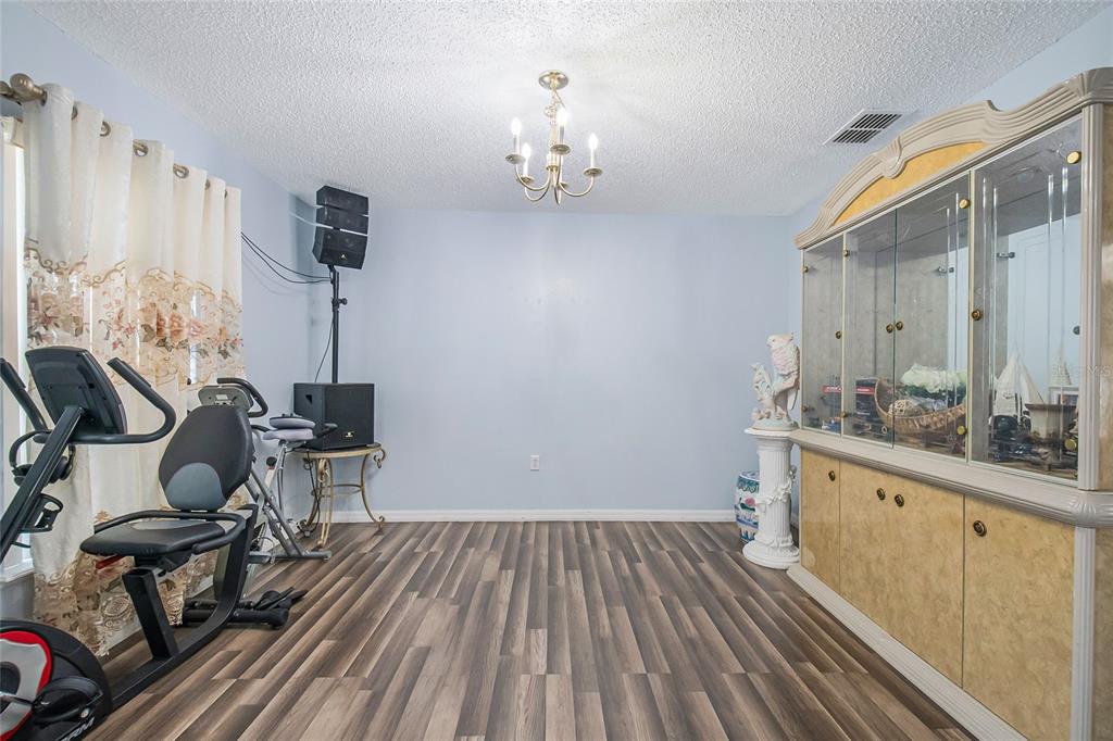 A dining room with wood-look flooring, a chandelier, a large china cabinet, and exercise equipment — 6 ALICANTE COURT, KISSIMMEE, FL