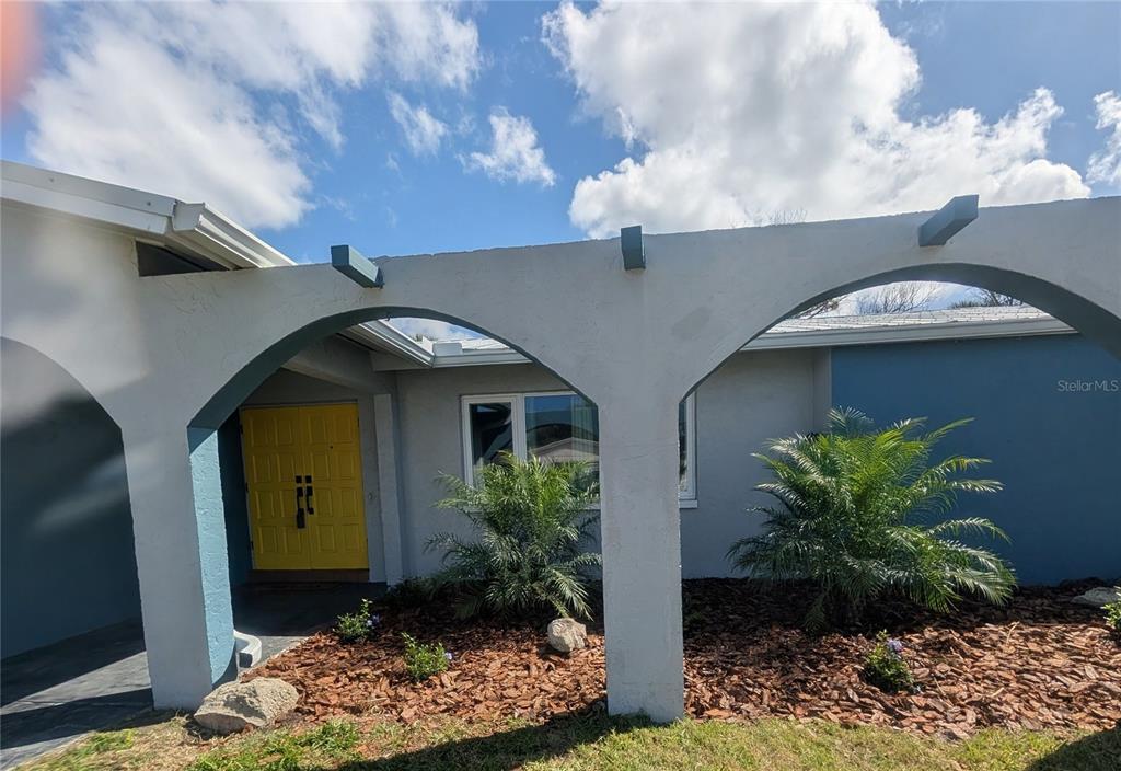 A house exterior features a yellow double door, arched entryway, and two small palm trees — 4723 114TH STREET N, MADEIRA BEACH, FL