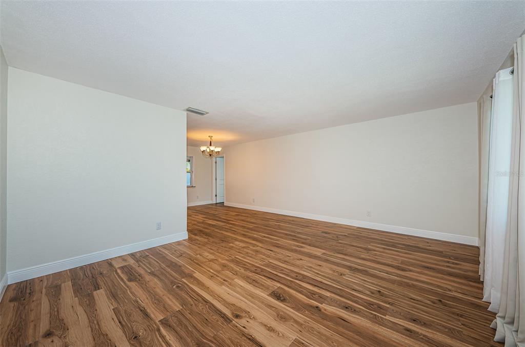 An empty room with wood-look flooring, white walls, and a view into an adjacent dining area — 4723 114TH STREET N, MADEIRA BEACH, FL