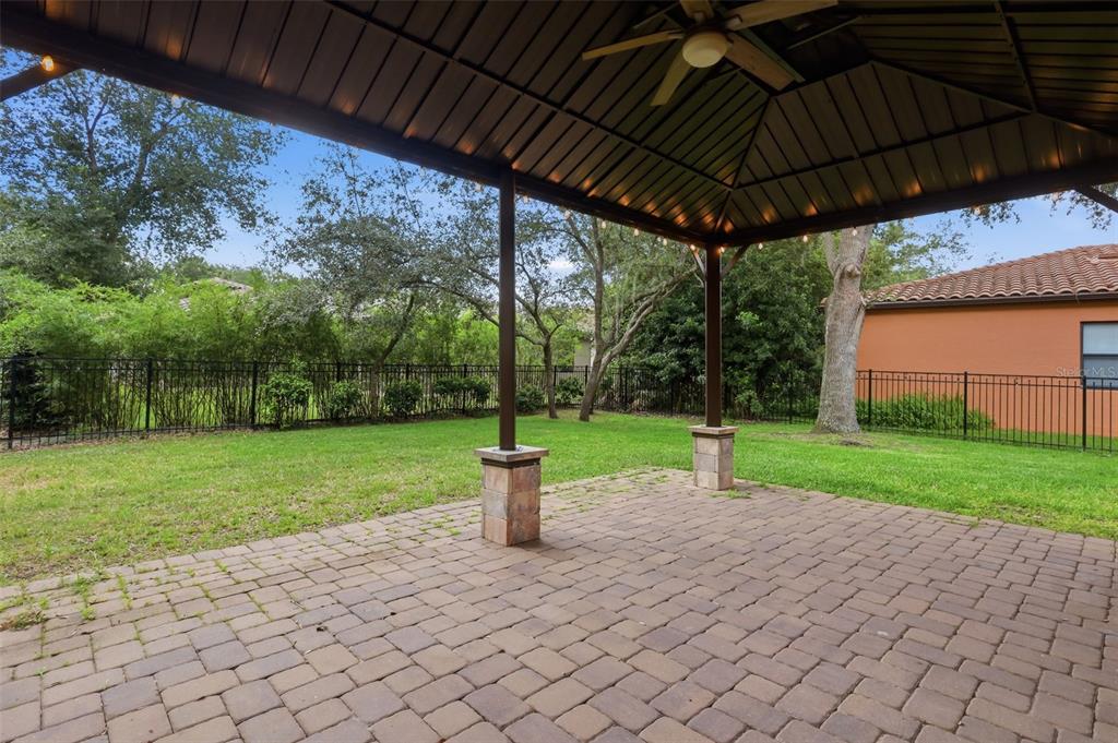 A covered patio with a metal roof, ceiling fan, and stone-based columns overlooks a backyard — 109 ELISSAR DRIVE, DEBARY, FL