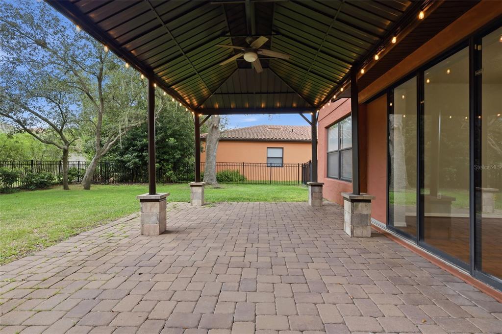 A covered patio with a metal roof, ceiling fan, and stone-based columns overlooks a backyard — 109 ELISSAR DRIVE, DEBARY, FL