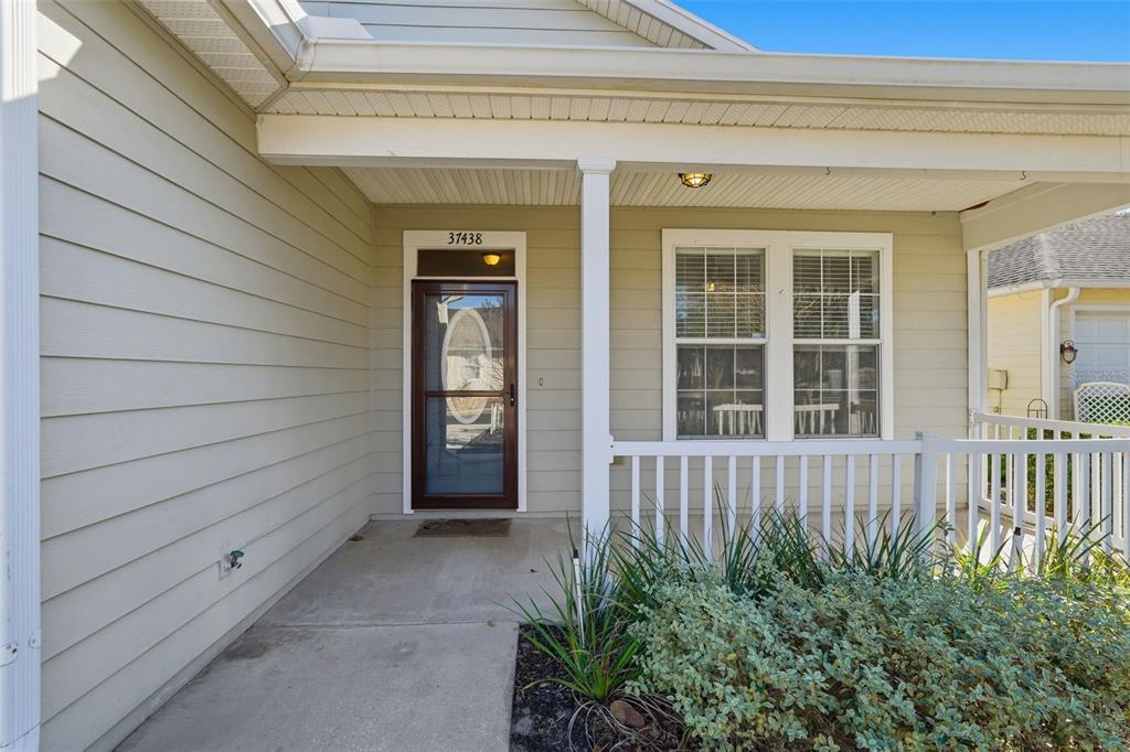 A covered front porch with a white railing leads to a glass-paneled entry door — 37438 PICKETTS MILL AVENUE, ZEPHYRHILLS, FL