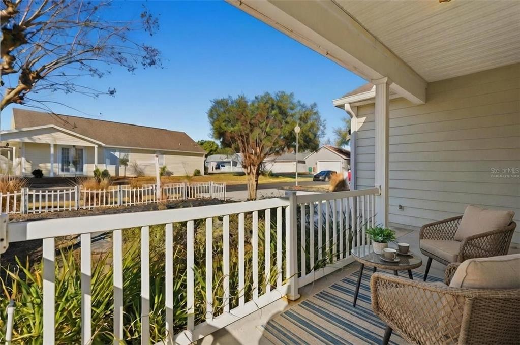 A covered porch features a white railing, outdoor seating, and a view of neighboring houses — 37438 PICKETTS MILL AVENUE, ZEPHYRHILLS, FL