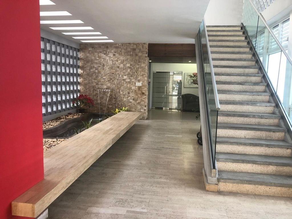A modern lobby features a stone accent wall, a water feature, and a glass-railed staircase — 1309 MAGDALENA, CONDADO, PR