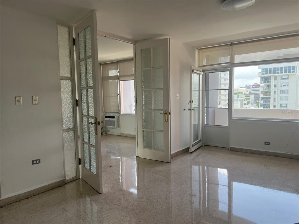 A bright room with polished tile floors, white French doors, and large windows overlooking buildings — 1309 MAGDALENA, CONDADO, PR