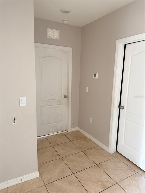 A small entryway with tan tile flooring, two white doors, and light gray walls — 615 TRALEE LANE, AUBURNDALE, FL