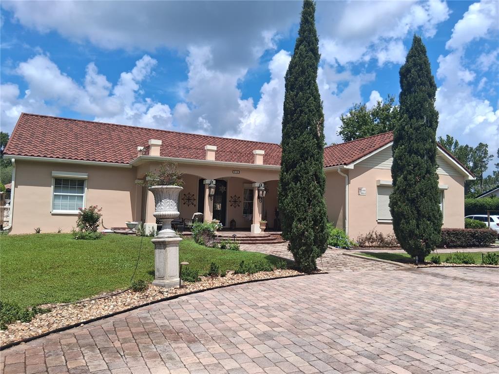 A single-story house with a tiled roof, beige stucco walls, and two tall cypress trees — 915 OLD WELCOME ROAD, LITHIA, FL