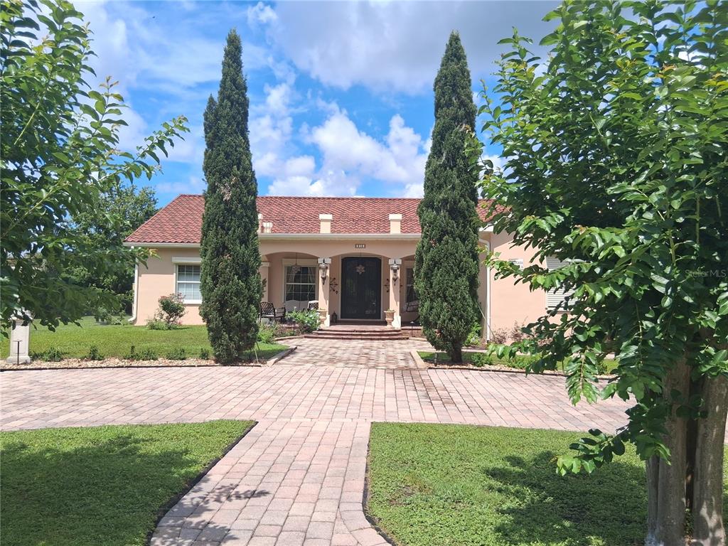 A single-story house with a tiled roof, brick driveway, and two tall cypress trees — 915 OLD WELCOME ROAD, LITHIA, FL