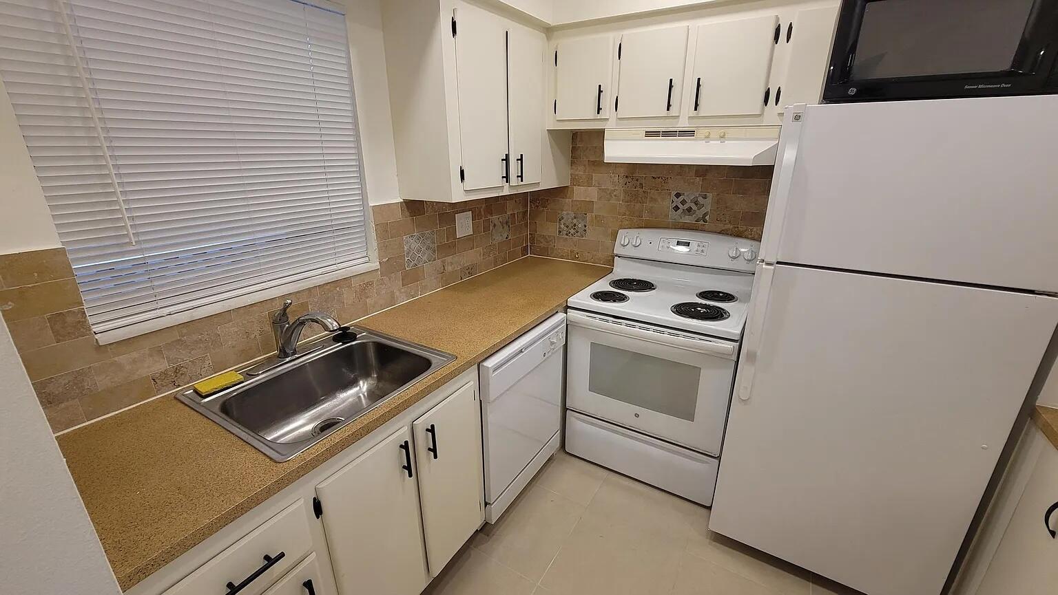 A kitchen features white cabinets, tan countertops, a stainless steel sink, and white appliances — 6501 Winfield Boulevard # 40, Margate FL 33063, MARGATE, FL