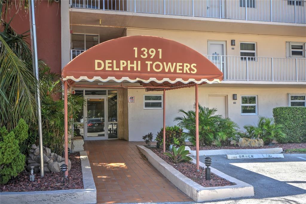 The exterior entrance of a multi-story apartment building features a brown awning with text — 1391 S Ocean Boulevard # 204, Pompano Beach FL 33062, POMPANO BEACH, FL