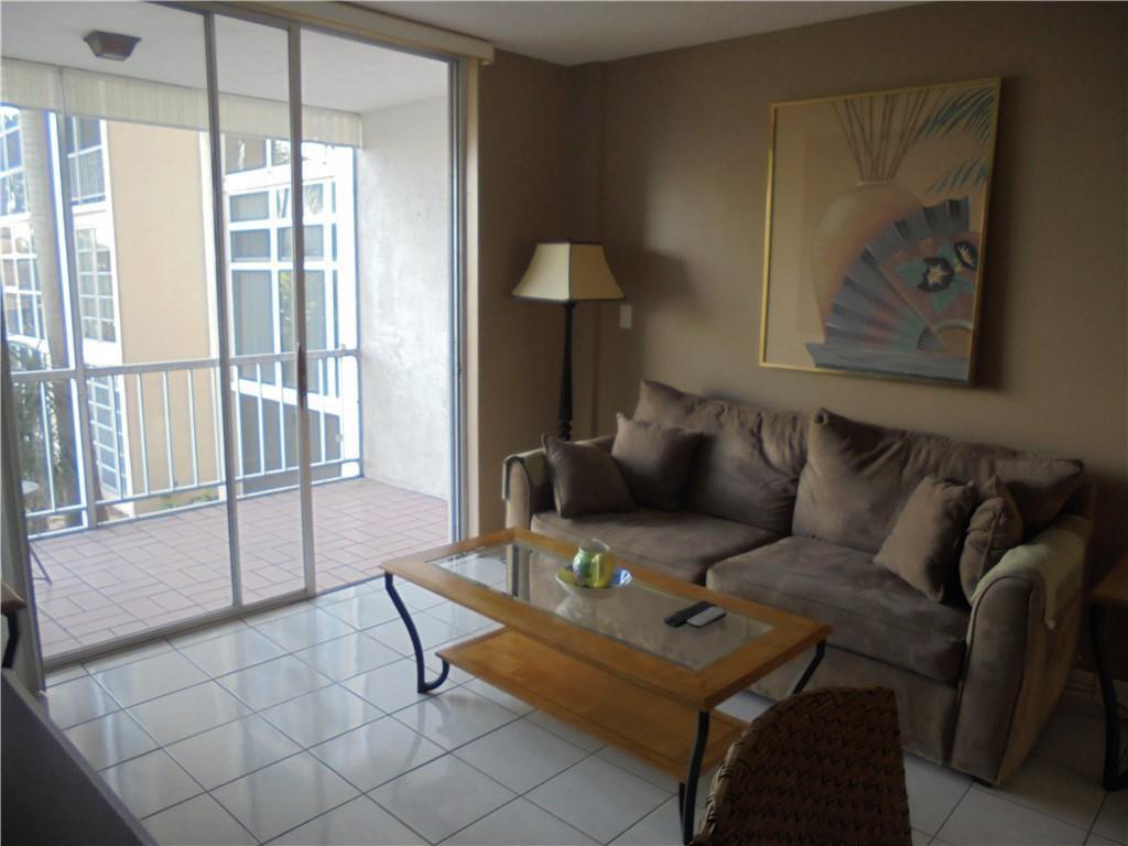 A living room features a brown sofa, a glass-topped coffee table, and a sliding balcony door — 1391 S Ocean Boulevard # 204, Pompano Beach FL 33062, POMPANO BEACH, FL