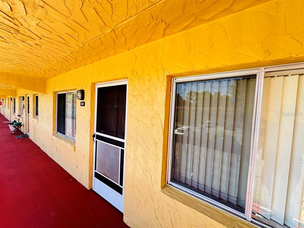 An exterior view of a yellow building with a red walkway and multiple unit doors — 400 EL CAMINO DRIVE UNIT 223, WINTER HAVEN, FL