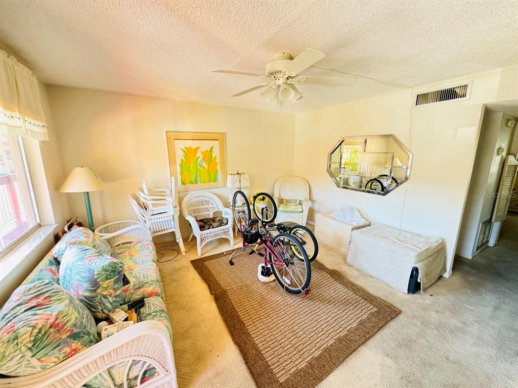 A living room features a floral sofa, a bicycle on a rug, and a ceiling fan — 400 EL CAMINO DRIVE UNIT 223, WINTER HAVEN, FL