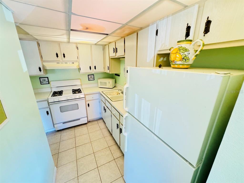 A kitchen features white appliances, light-colored cabinets, and tile flooring — 400 EL CAMINO DRIVE UNIT 223, WINTER HAVEN, FL