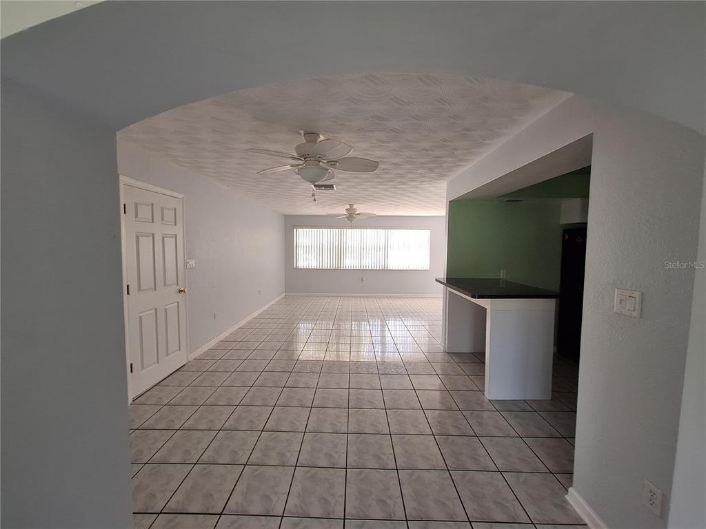 A room with light-colored tile flooring, two ceiling fans, and a kitchen pass-through counter — 22191 NEW ROCHELLE AVENUE, PORT CHARLOTTE, FL