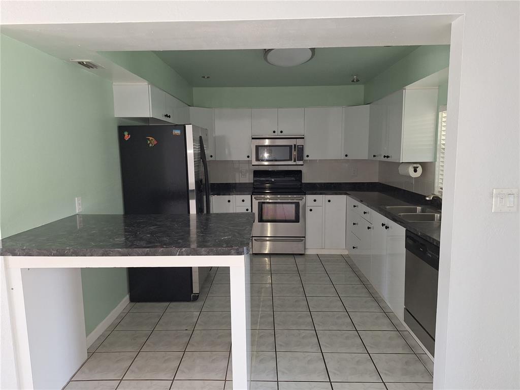 A kitchen features white cabinets, stainless steel appliances, dark countertops, and light-colored tile flooring — 22191 NEW ROCHELLE AVENUE, PORT CHARLOTTE, FL