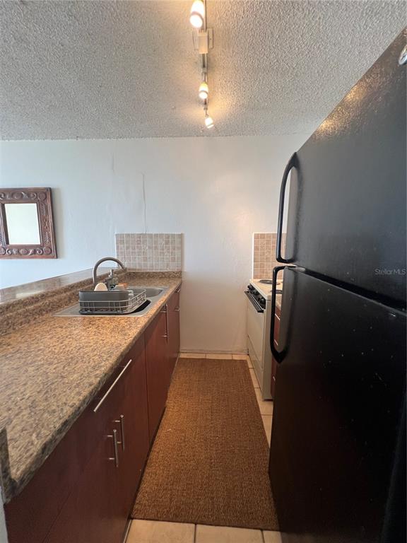 A galley kitchen features dark wood cabinets, speckled laminate countertops, and black appliances — 16 AMAPOLA UNIT 504, CAROLINA, PR