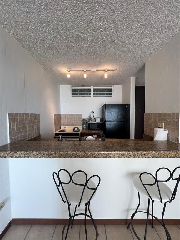 A kitchen with a breakfast bar, two stools, and a black refrigerator — 16 AMAPOLA UNIT 504, CAROLINA, PR