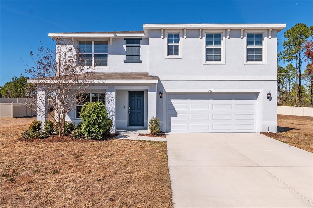 A two-story house with a white stucco exterior, a dark blue front door, and a garage — 7179 SW 135TH PLACE, OCALA, FL