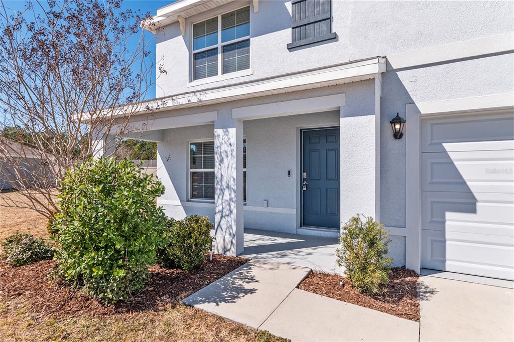 A two-story house exterior features a blue front door, a covered porch, and a garage — 7179 SW 135TH PLACE, OCALA, FL
