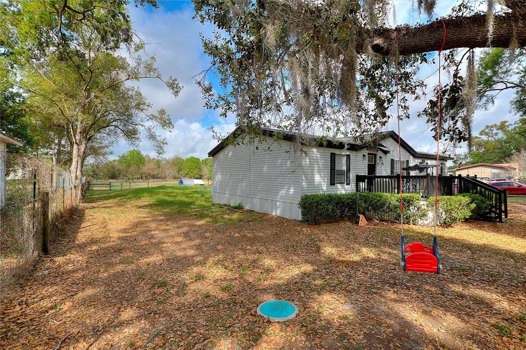 A white mobile home sits on a grassy lot with a red swing hanging from a tree — 3309 COOPER ROAD, PLANT CITY, FL