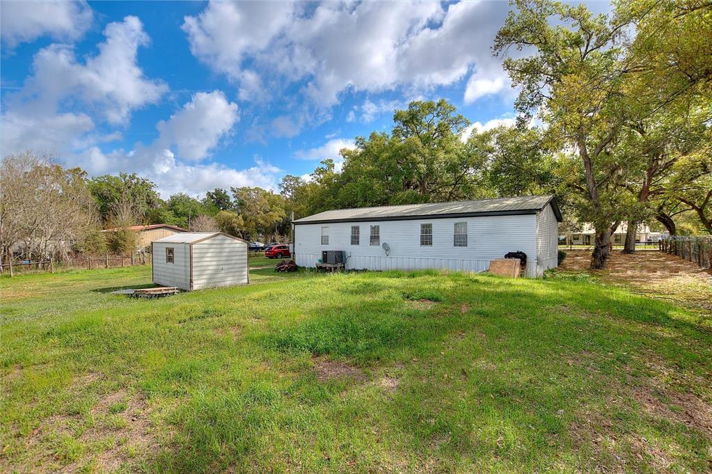 A white mobile home and a small metal shed sit on a grassy, tree-lined lot — 3309 COOPER ROAD, PLANT CITY, FL