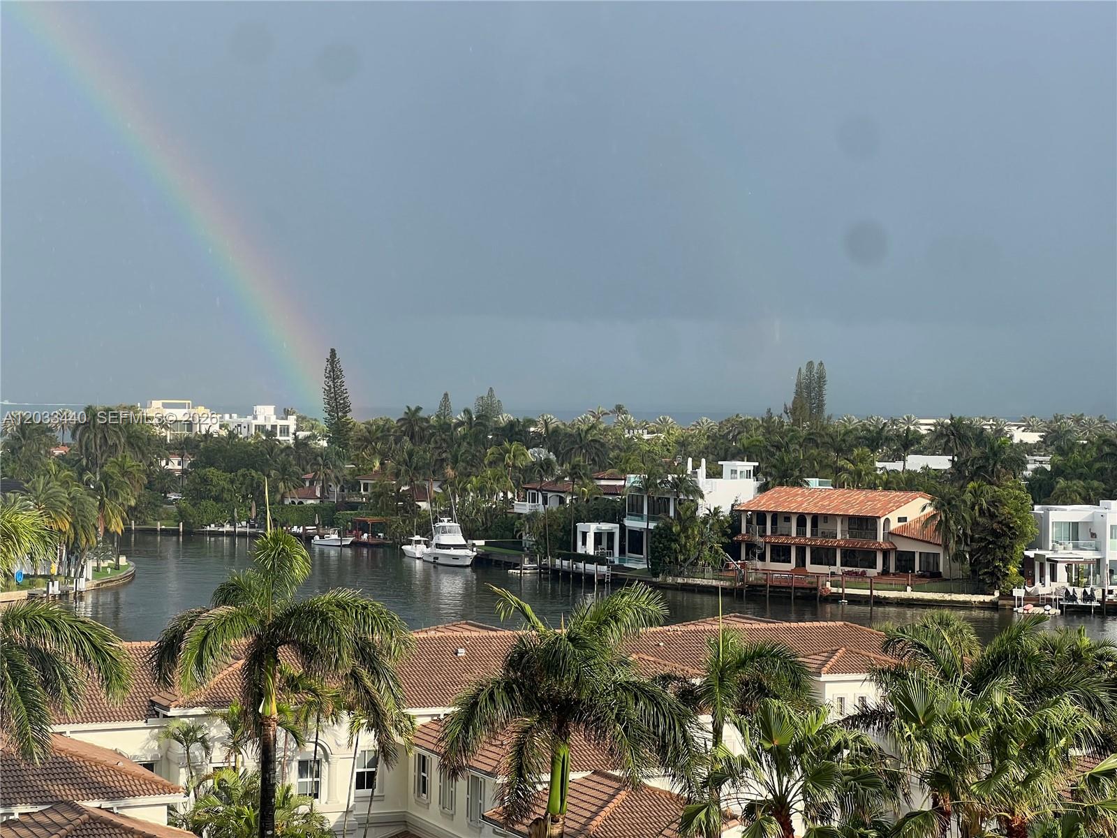 A view of a canal with boats, houses, and palm trees under a rainbow — 21050 Point Pl # 702, Aventura FL 33180, AVENTURA, FL