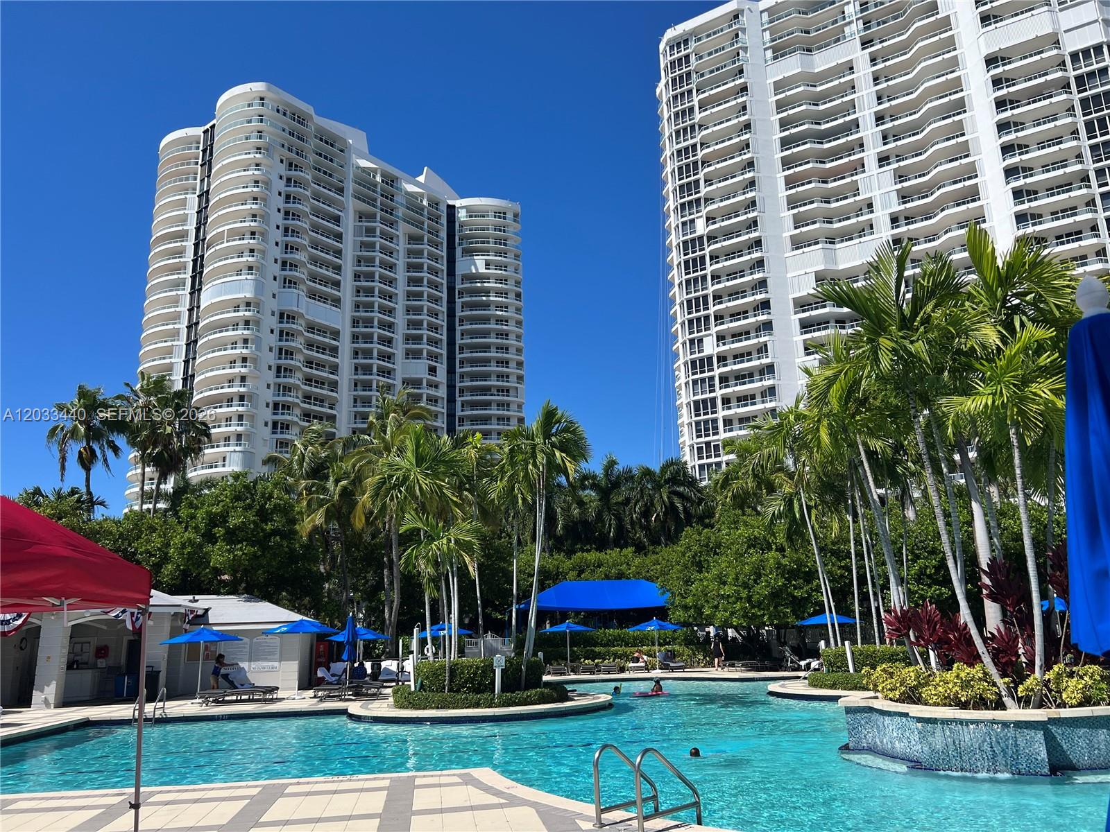 A swimming pool sits in front of two tall white residential towers and palm trees — 21050 Point Pl # 702, Aventura FL 33180, AVENTURA, FL