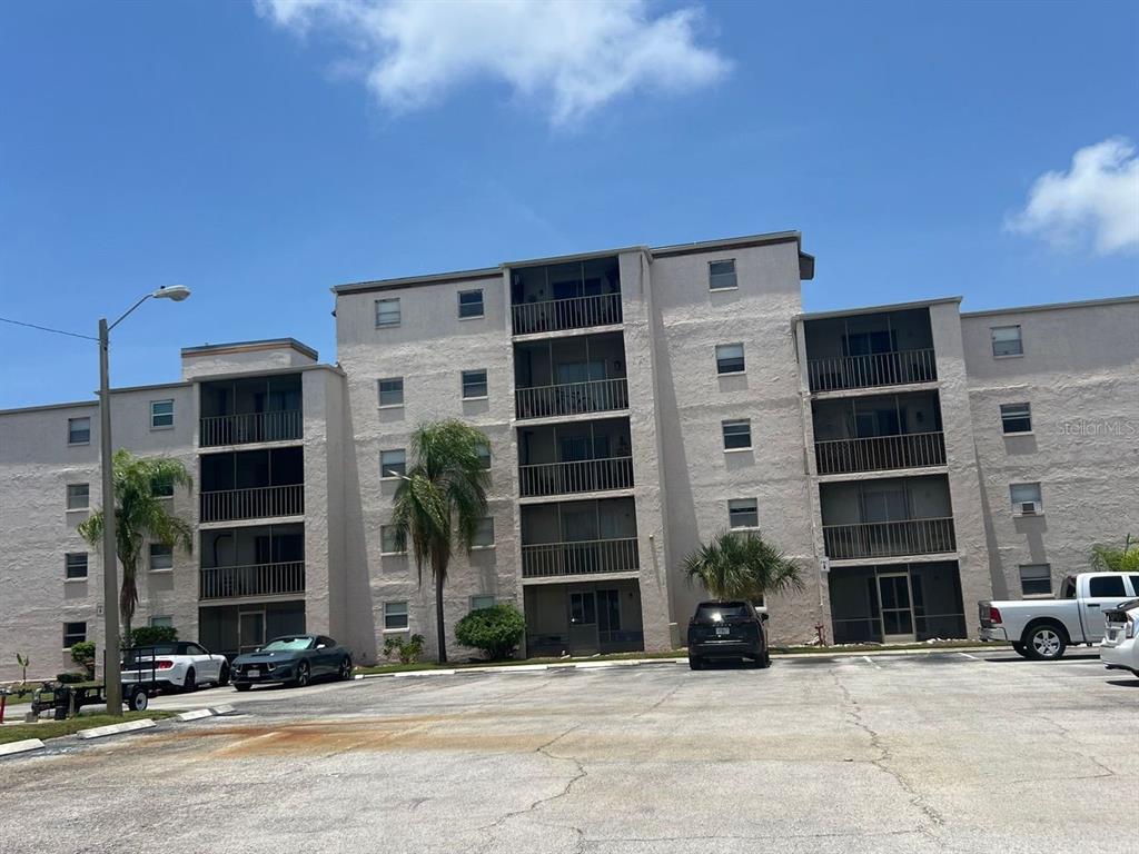 A multi-story apartment building with screened balconies and a parking lot in front — 5541 BAY BOULEVARD UNIT 107, PORT RICHEY, FL