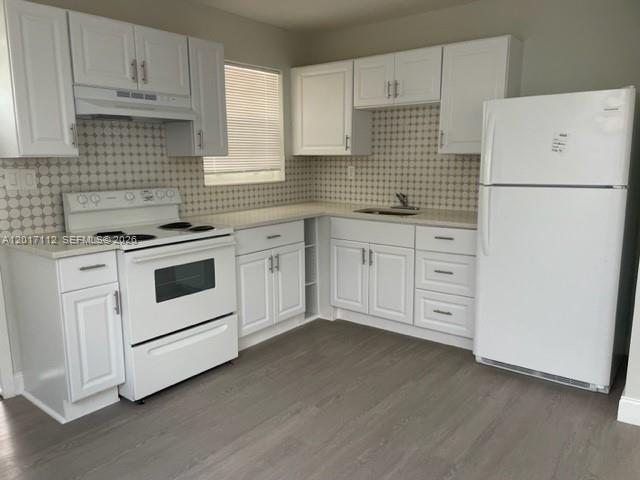A kitchen features white cabinets, white appliances, a patterned backsplash, and light wood-look flooring — FORT LAUDERDALE, FL