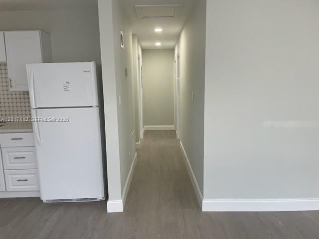 A white refrigerator stands next to a hallway with light-colored flooring and walls — FORT LAUDERDALE, FL