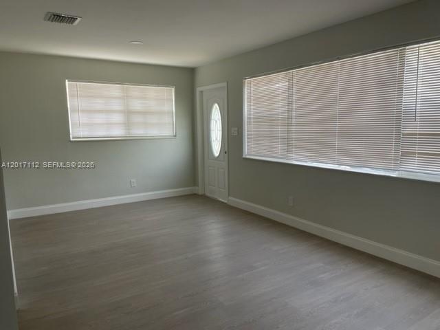 An empty room features light-colored wood flooring, gray walls, and large windows with blinds — FORT LAUDERDALE, FL