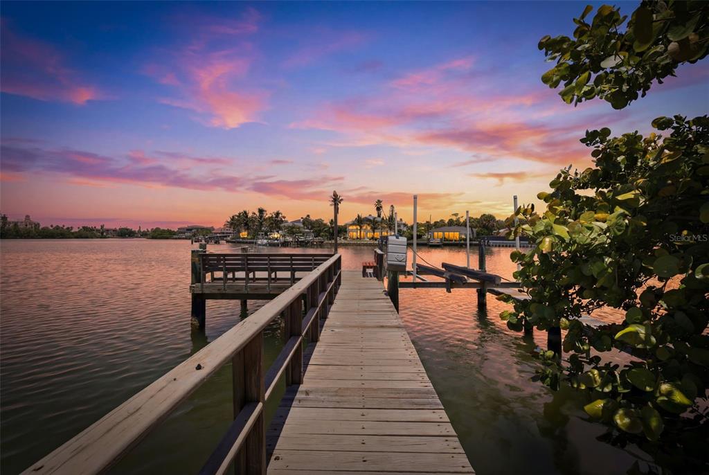 A wooden dock extends over calm water toward a sunset sky and distant waterfront homes — 3666 BELLE VISTA DRIVE E, ST PETERSBURG, FL