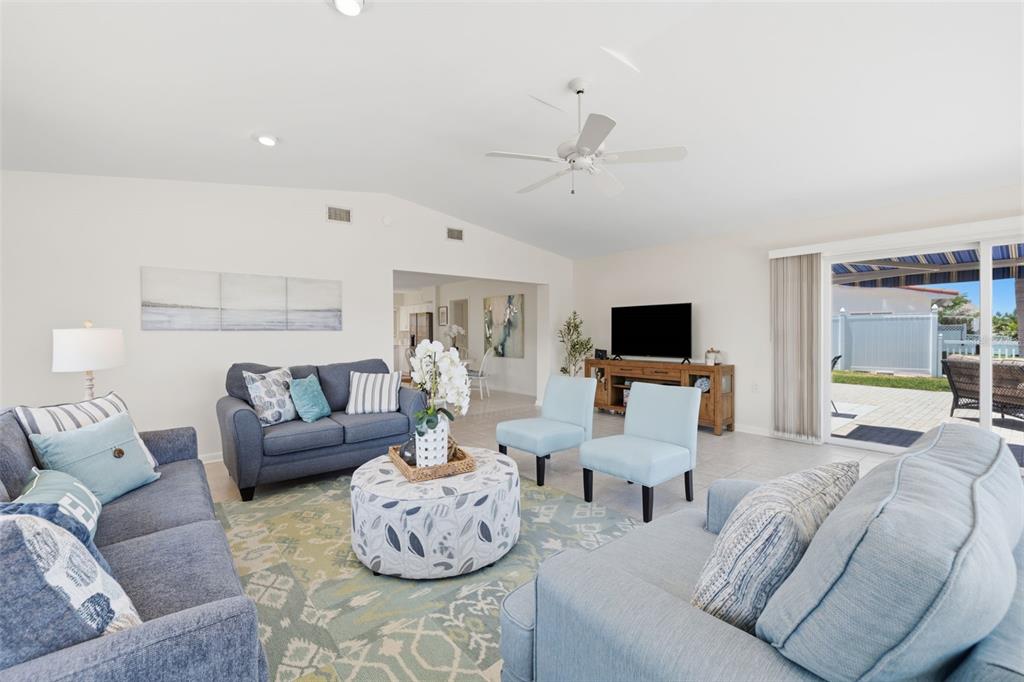 A bright living room features blue sofas, light blue accent chairs, and a sliding glass door — 3666 BELLE VISTA DRIVE E, ST PETERSBURG, FL