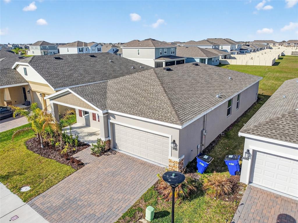 An aerial view of a suburban house with a gray roof, tan stucco, and paver driveway — 2619 PEACE OF MIND AVENUE, KISSIMMEE, FL