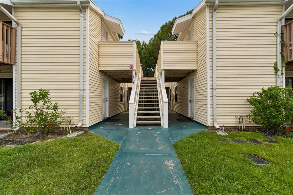 A two-story apartment building exterior features light yellow siding, a central staircase, and green walkways — 133 SABAL COURT UNIT G, OLDSMAR, FL