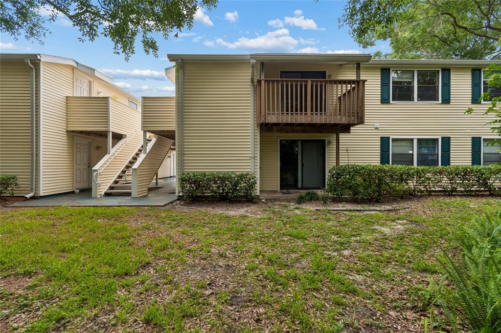 The exterior of a two-story apartment building features yellow siding, a wooden balcony, and stairs — 133 SABAL COURT UNIT G, OLDSMAR, FL