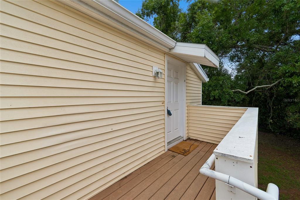 A wooden deck with a white railing leads to a door on a yellow-sided building — 133 SABAL COURT UNIT G, OLDSMAR, FL