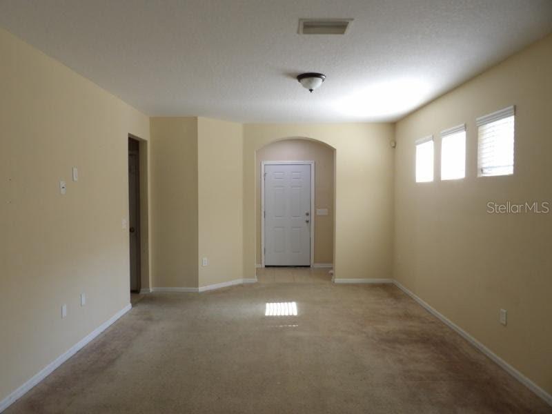 An empty living room features beige walls, tan carpeting, and a white front door — 12669 BELCROFT DRIVE, RIVERVIEW, FL
