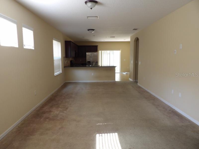 This open-concept living area features beige carpet, light-colored walls, and a kitchen with dark cabinetry — 12669 BELCROFT DRIVE, RIVERVIEW, FL