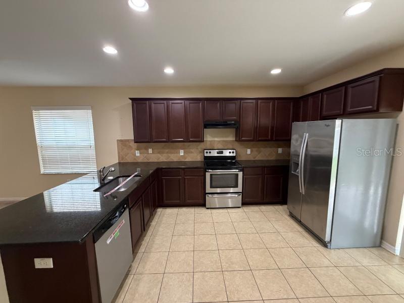 A kitchen features dark wood cabinets, black countertops, stainless steel appliances, and beige tile flooring — 12669 BELCROFT DRIVE, RIVERVIEW, FL